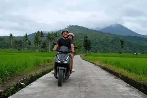 A couple rides a scooter on a road between rice fields